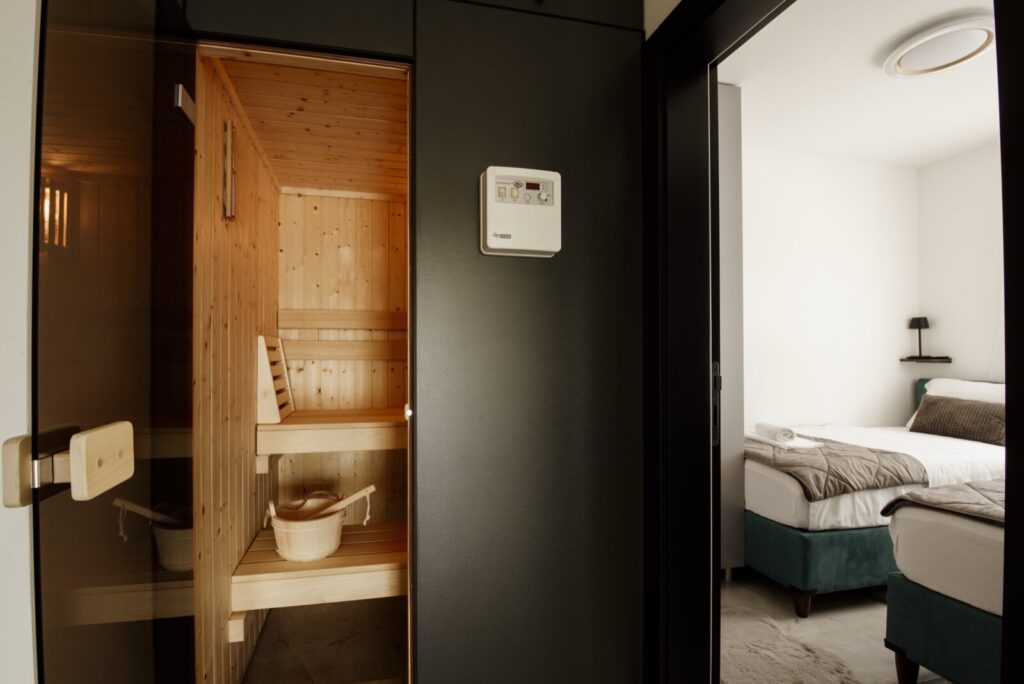 A home sauna cabin installed beside a bedroom with a wall-mounted control unit